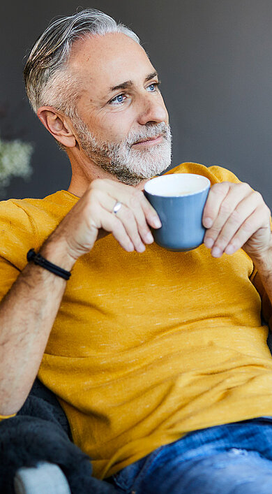 Raeds Eigentumswohnungen Hamburg Altona. Mann sitzt entspannt in seinem Wohnzimmer und trinkt einen Kaffee.